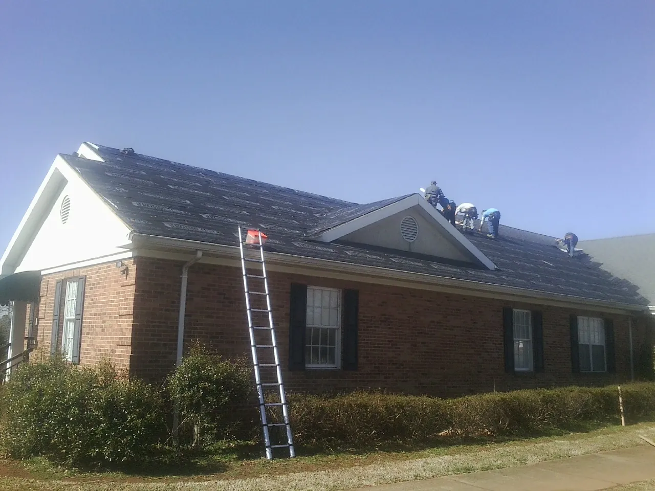 Crew tearing shingles off a brick ranch roof with a ladder set — Metal Roof Repair work by our crew in Rogersville