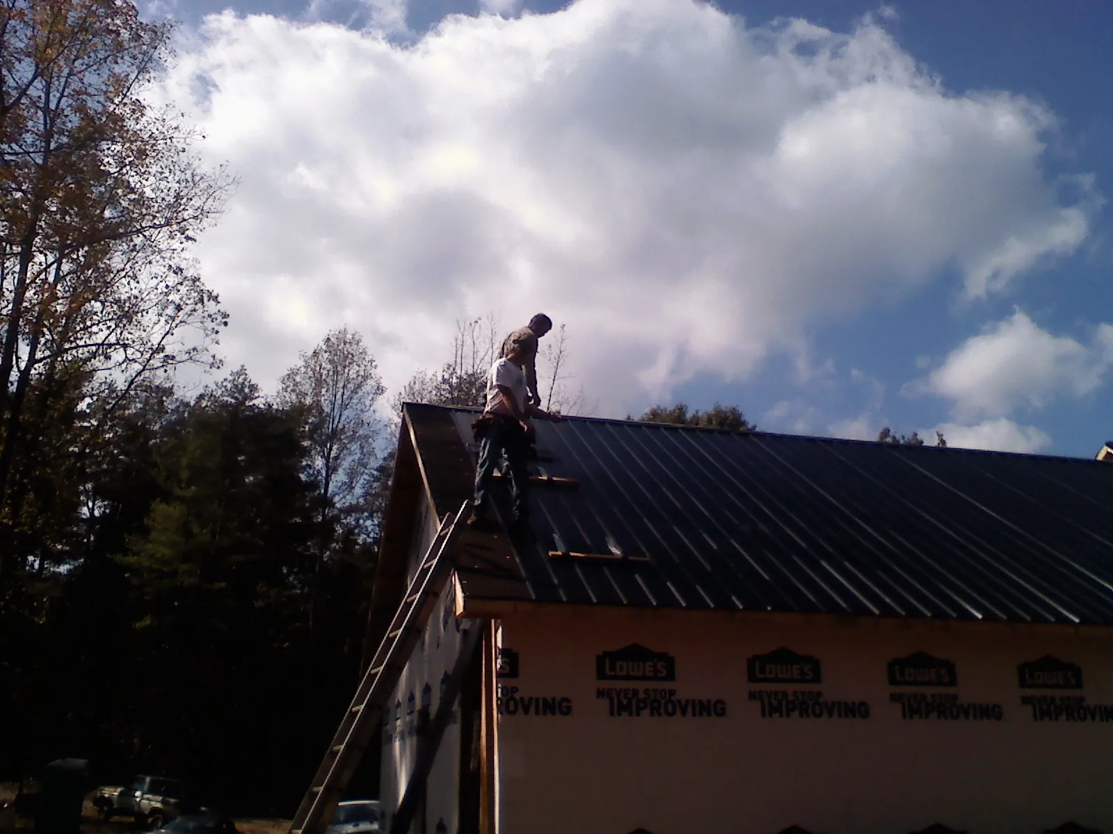 Roofer fastening dark metal panels high against a cloudy sky, from a Roof Inspection job in Rogersville