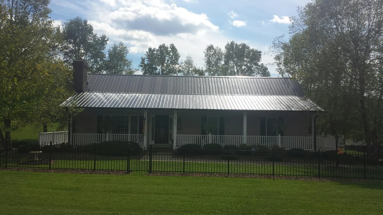 Gray metal roof on a brick ranch with a full width front porch — Gutter Guard Installation work by our crew in Rogersville